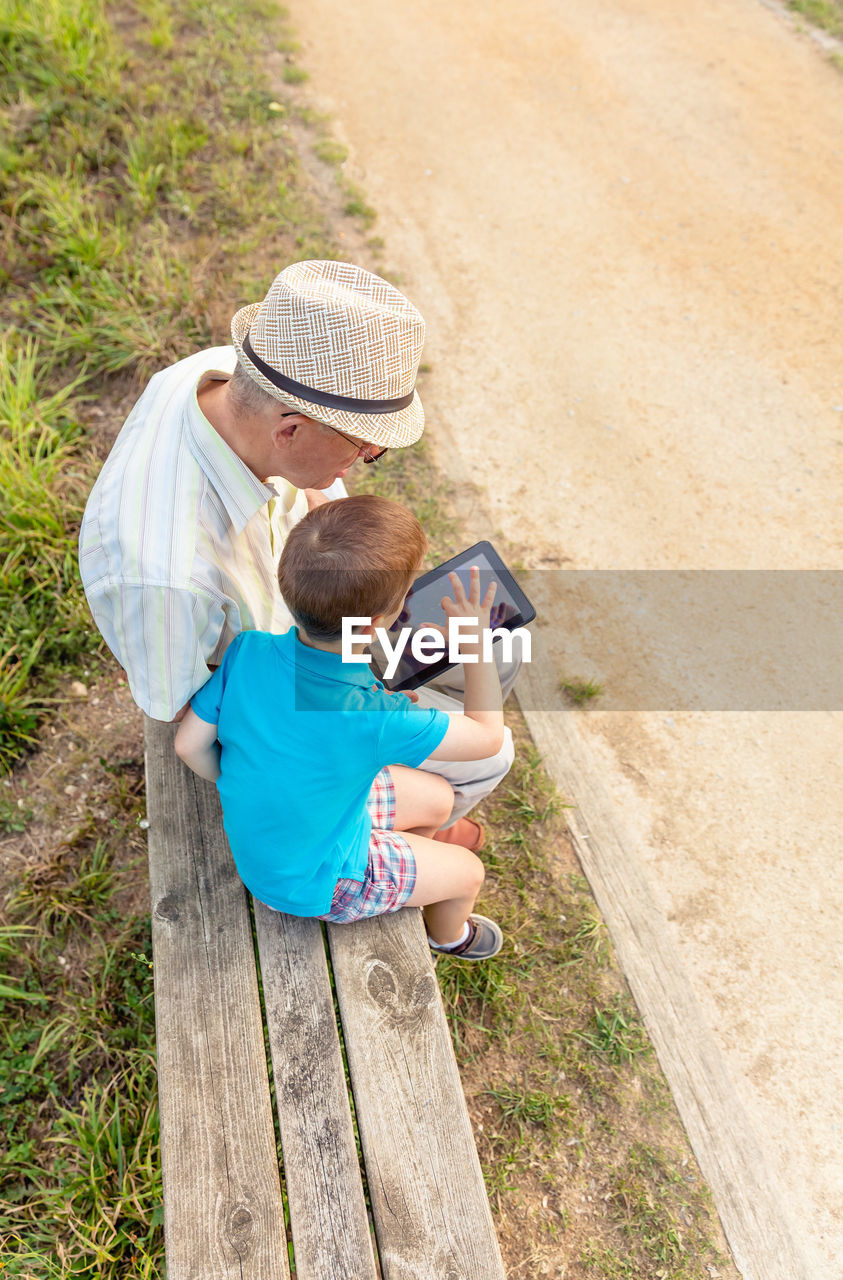 Grandson teaching digital tablet to grandfather while sitting in public park