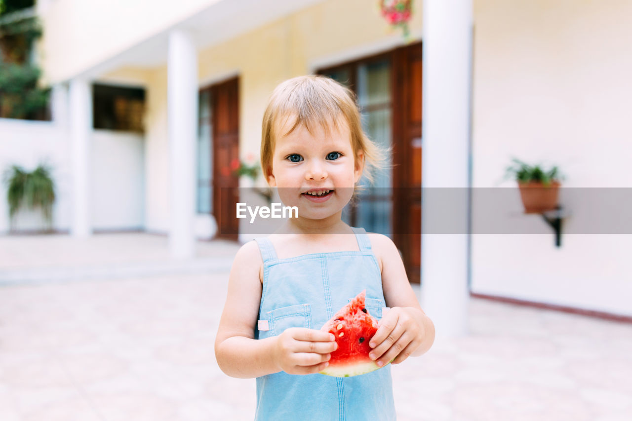 Little cute cheerful girl eating a slice of watermelon close up.