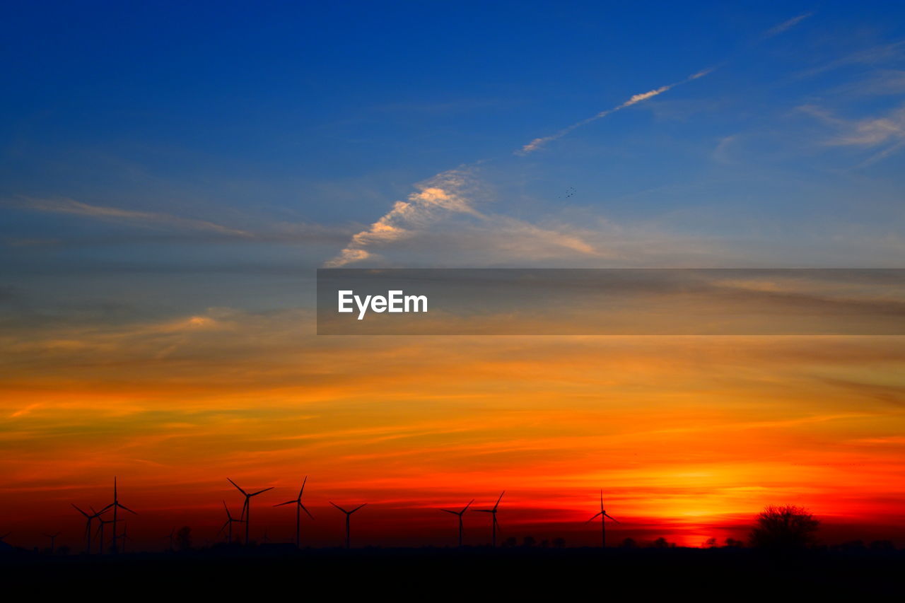 SILHOUETTE OF WIND TURBINES AGAINST ORANGE SKY