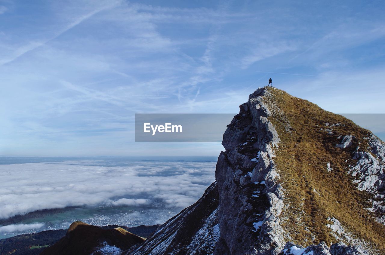 Person standing on mountain peak against sky