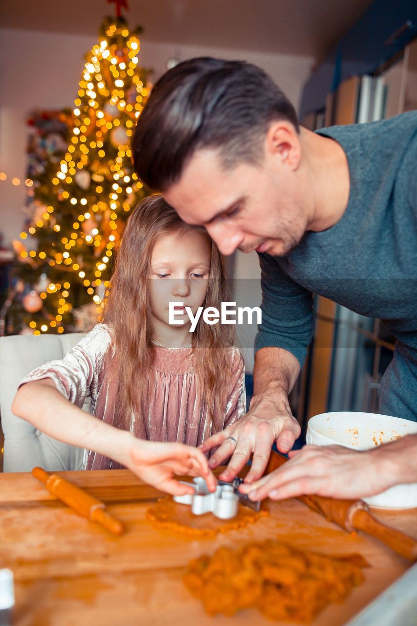 Father assisting daughter in making christmas cookies on table at home