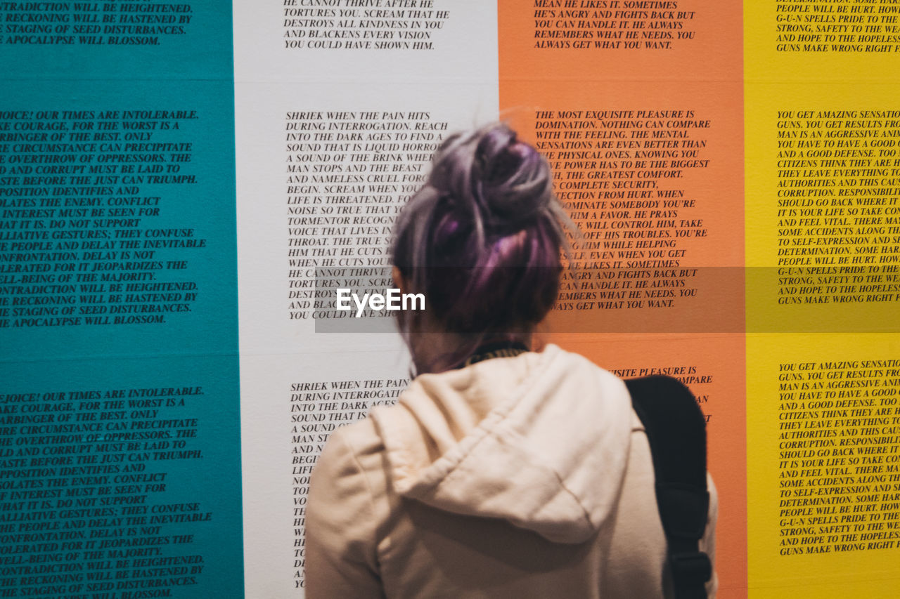 REAR VIEW PORTRAIT OF A WOMAN STANDING AGAINST TEXT