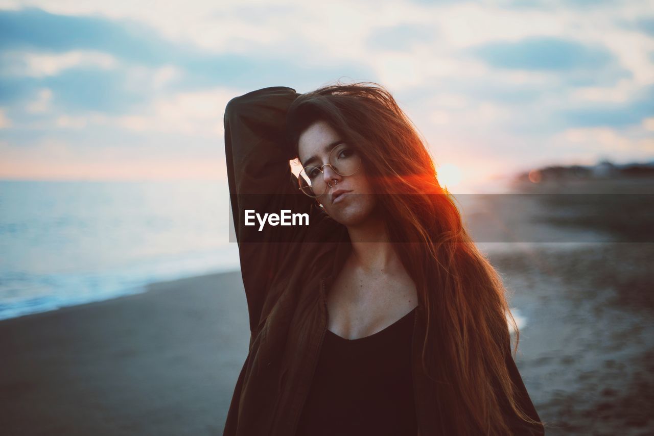 Portrait of young woman standing at beach during sunset