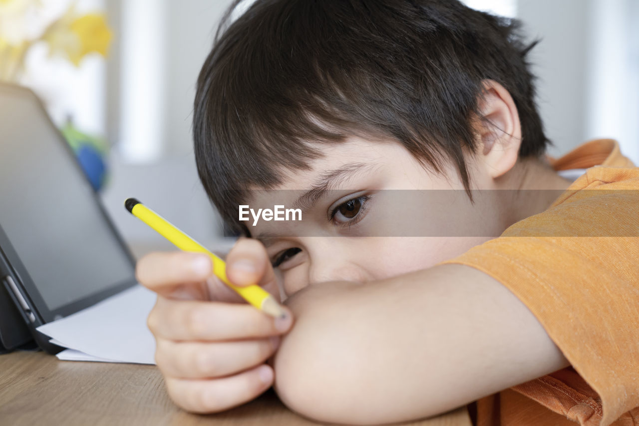 Close-up of bored boy lying on table at home