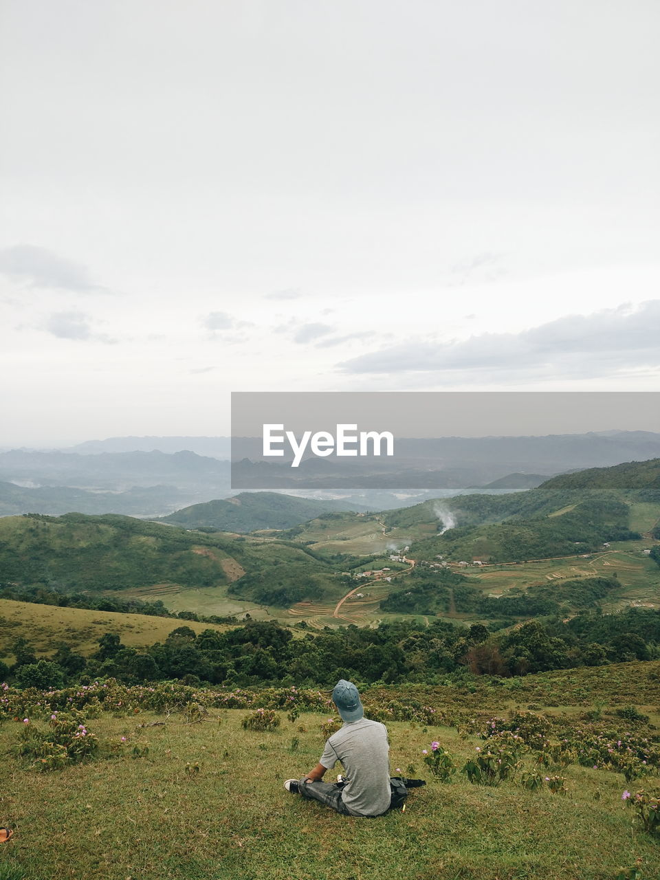 Rear view of man sitting on landscape against sky