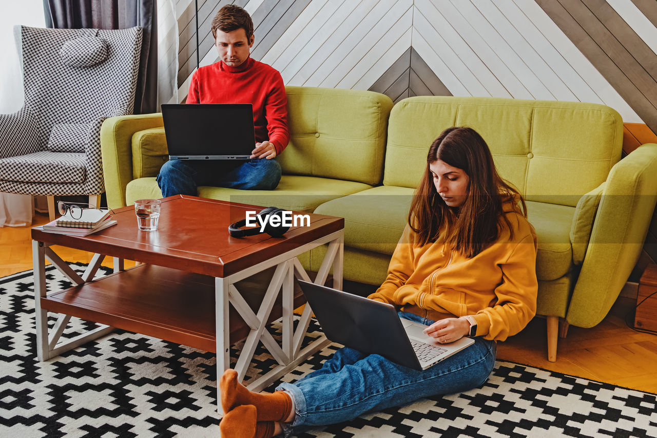 Couple working at home on their laptops in cozy stylish living room. modern lifestyle, remote work