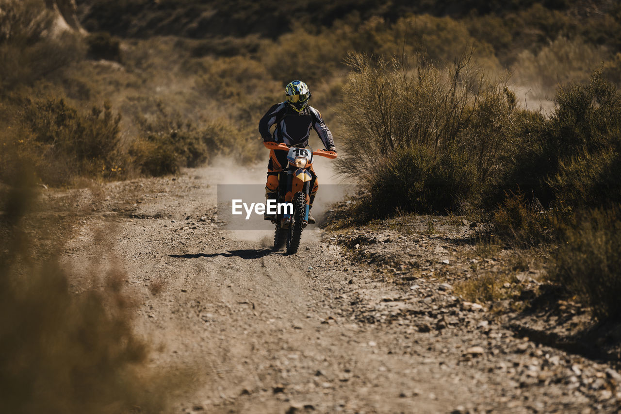 Male biker with protective sportswear riding motorcycle on dirt road