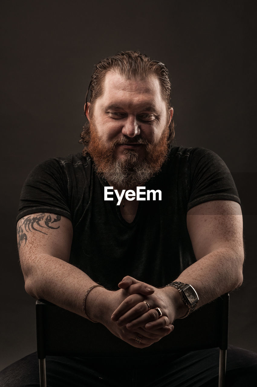 PORTRAIT OF MATURE MAN SITTING OVER BLACK BACKGROUND