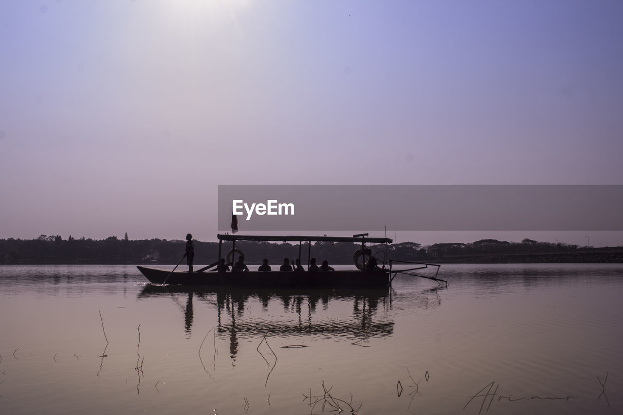 People on boat in lake against clear sky