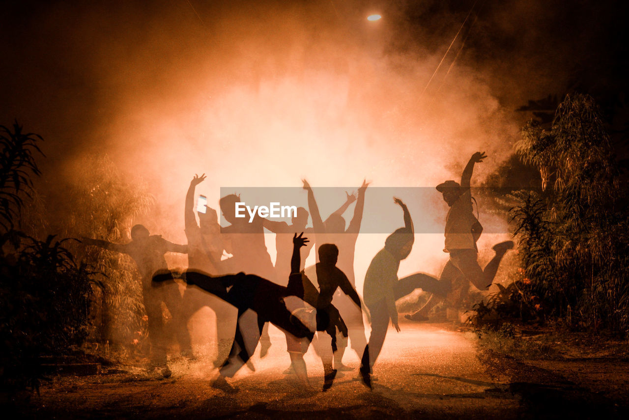 Digital composite image of people jumping over street in foggy weather at night