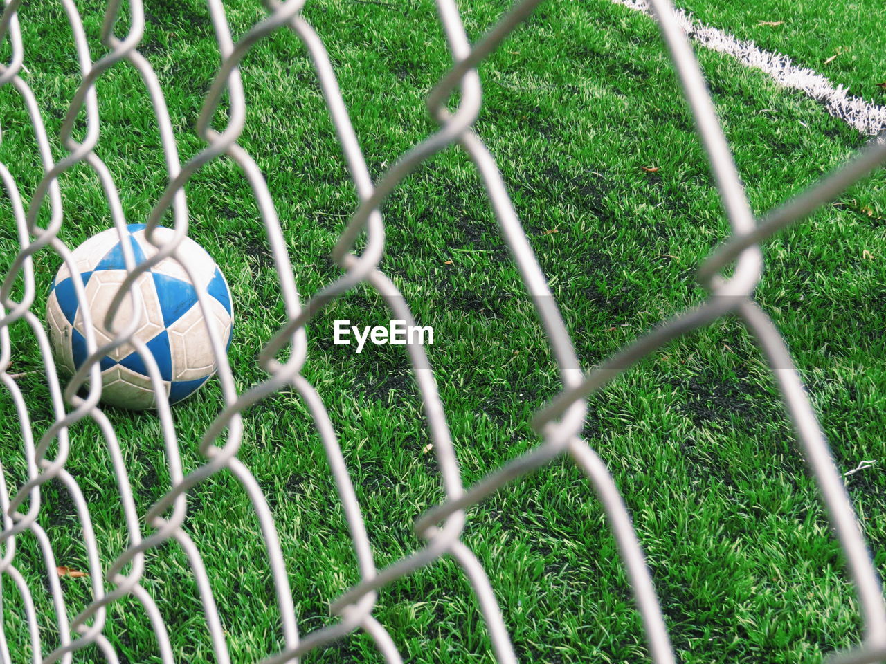 Soccer ball on field seen through chainlink fence