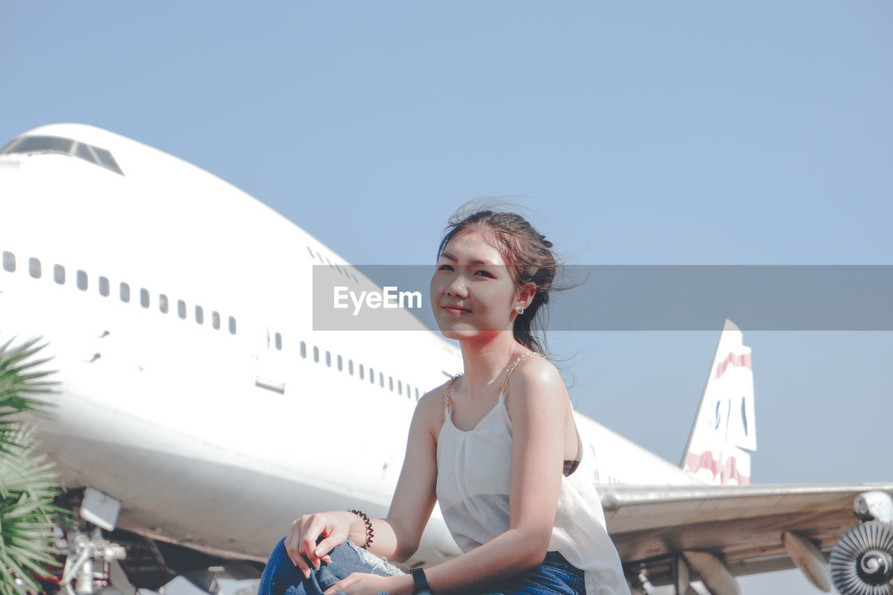 Smiling woman sitting against airplane