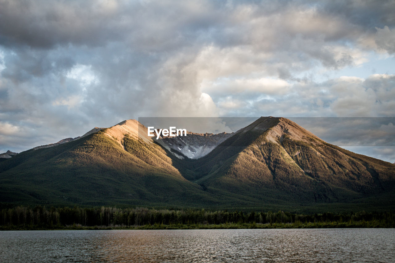 View of lake by mountains against cloudy sky