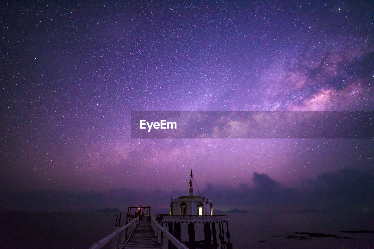 Pier over sea against milky way at night