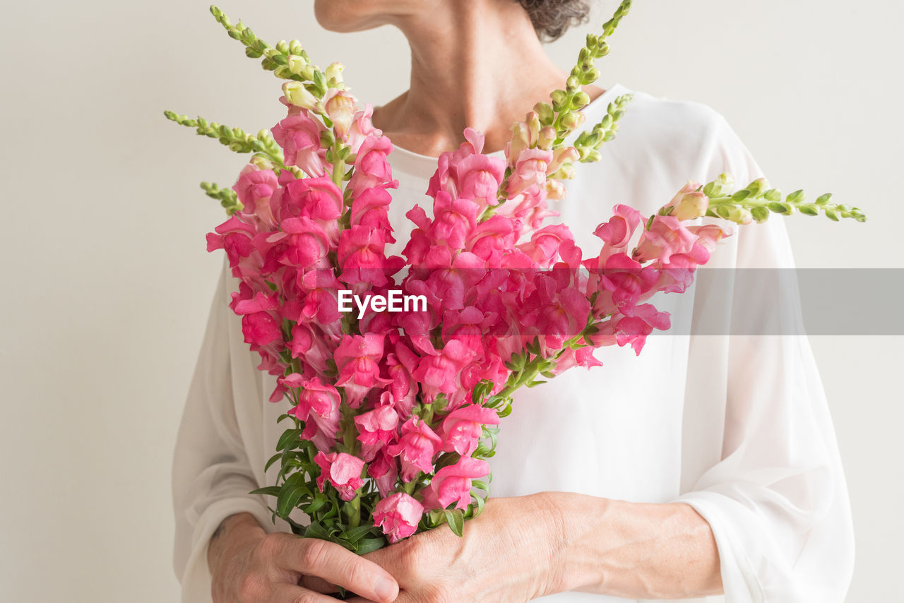 Midsection of woman holding pink flowers against wall