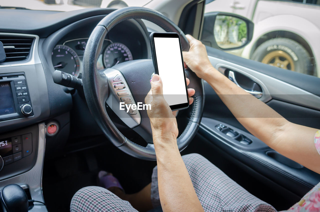 Low section of woman holding smartphone while driving car on road at city