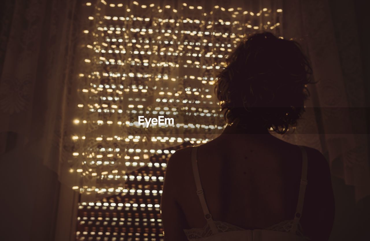 Rear view of woman standing by curtain at home