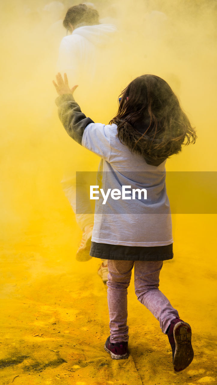 Rear view of girl enjoying with yellow powder paint