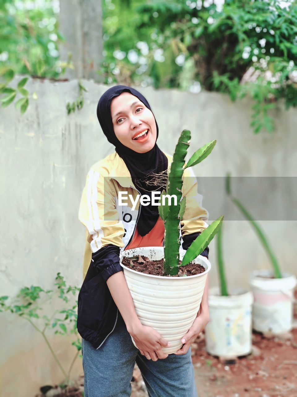 Portrait of smiling woman holding potted plant while standing in yard