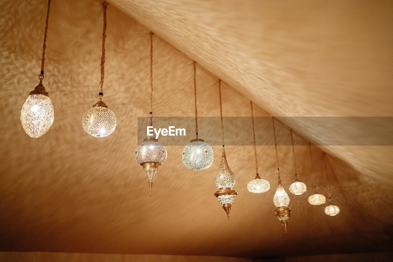 From below of various bright glowing lanterns in traditional moroccan style hanging under ceiling in room