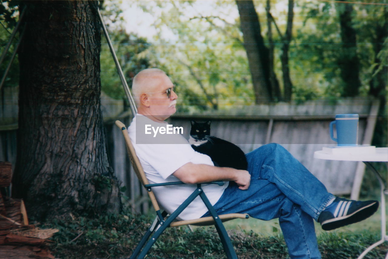 Senior man with cat sitting on chair at yard