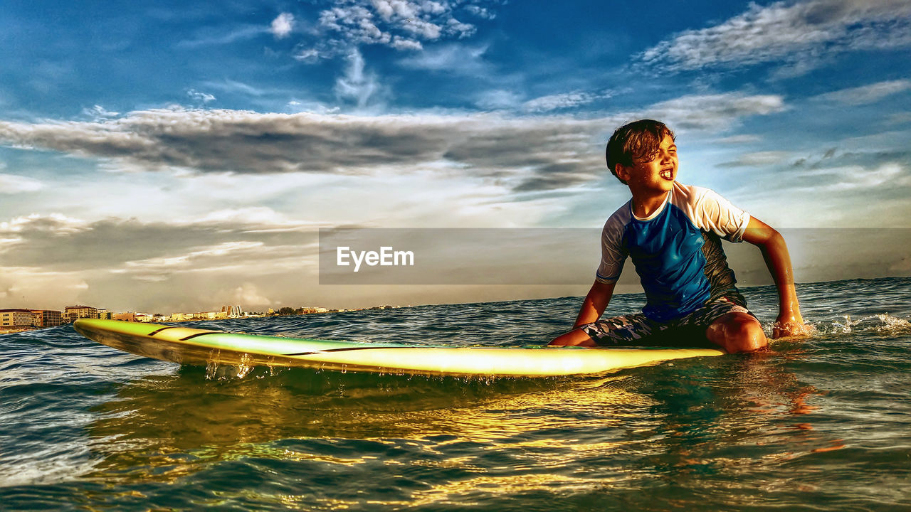 Boy on surfboard in sea against sky