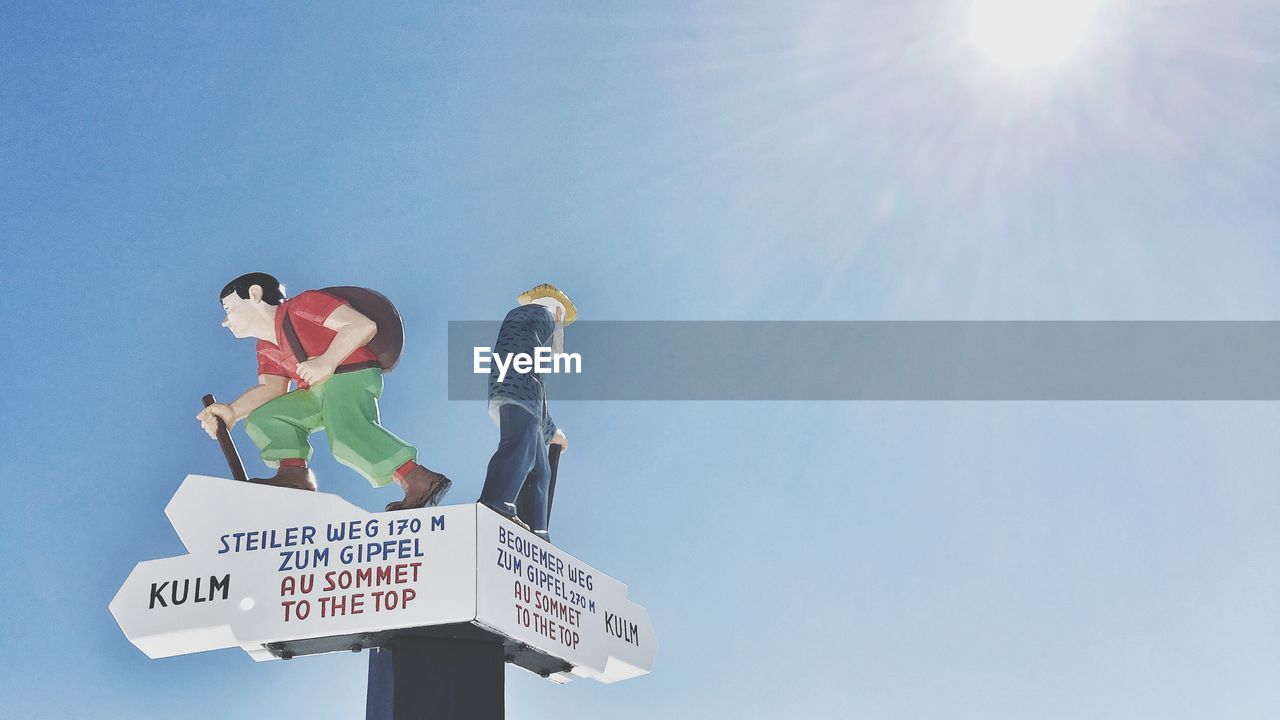 Low angle view of sign board and sculptures against sky