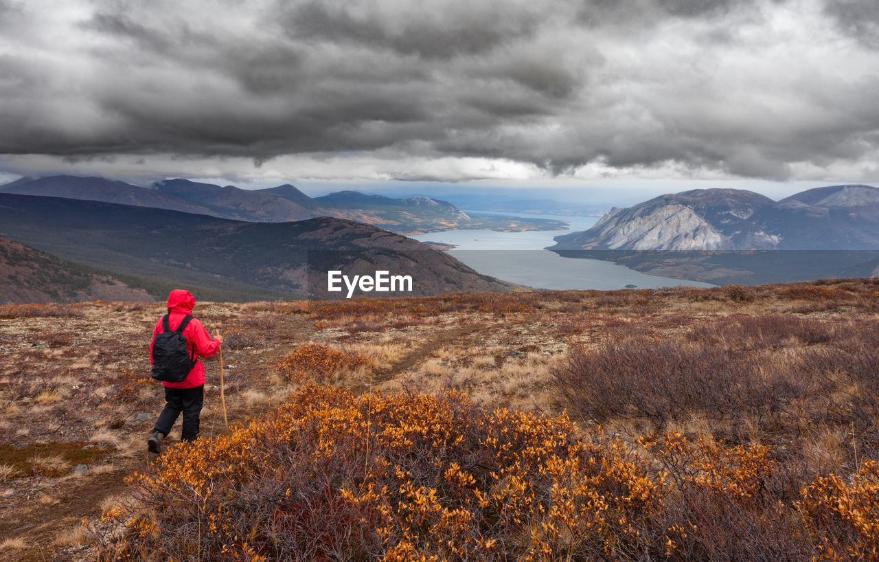 Rear view of woman hiking on mountain against cloudy sky