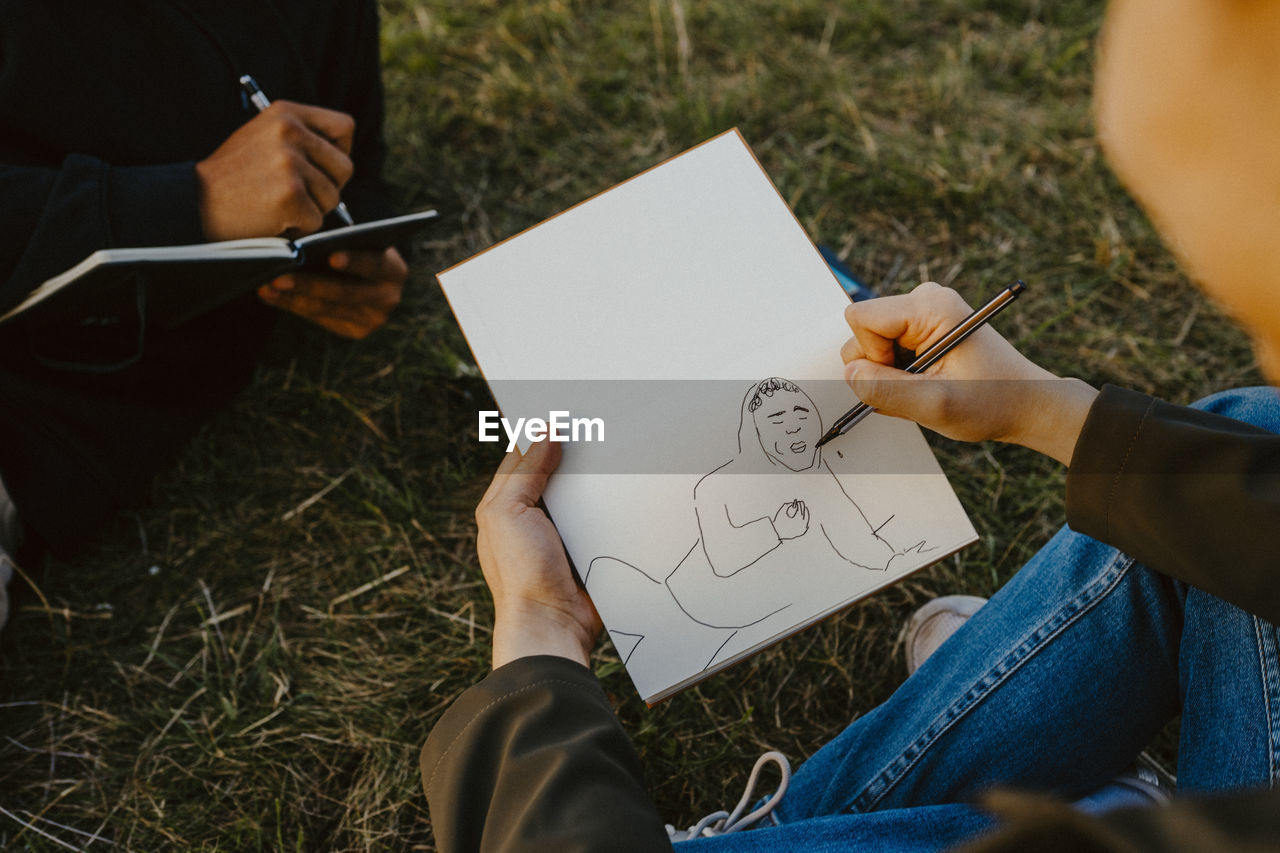 Cropped image of man's hands sketching in book at park