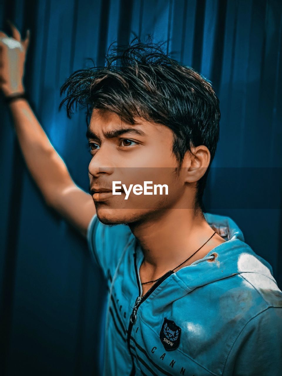 PORTRAIT OF YOUNG MAN LOOKING AWAY AGAINST BLUE WALL