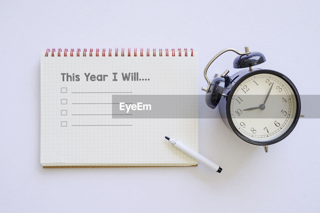 High angle view of alarm clock with diary and pen on white background