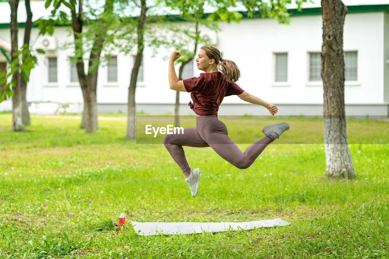 Beautiful girl athlete in sportswear jumps high in the park or in the yard of her house