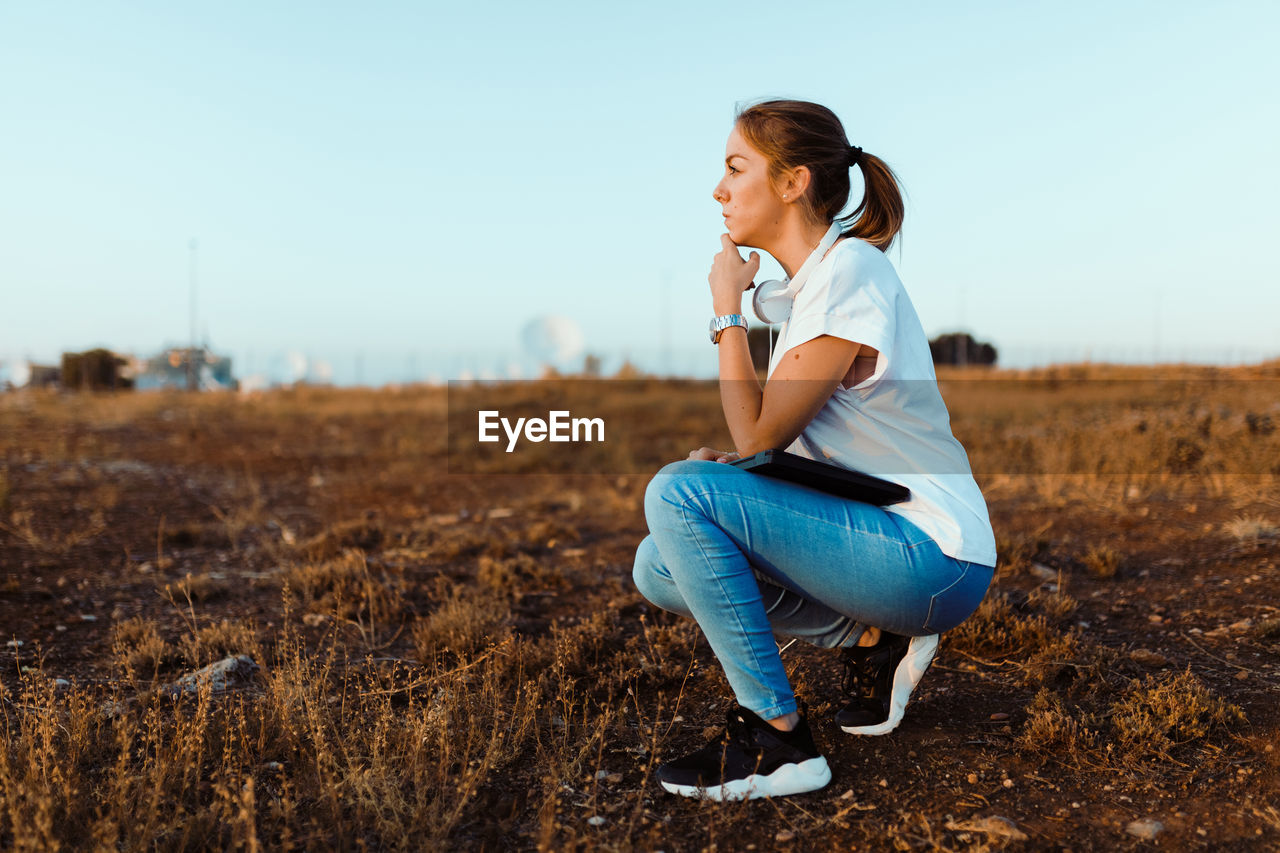 SIDE VIEW OF WOMAN SITTING ON FIELD