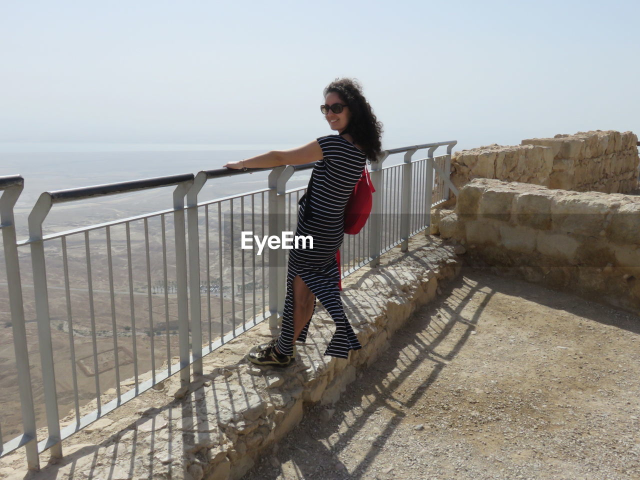 Portrait of woman standing by railing against sky