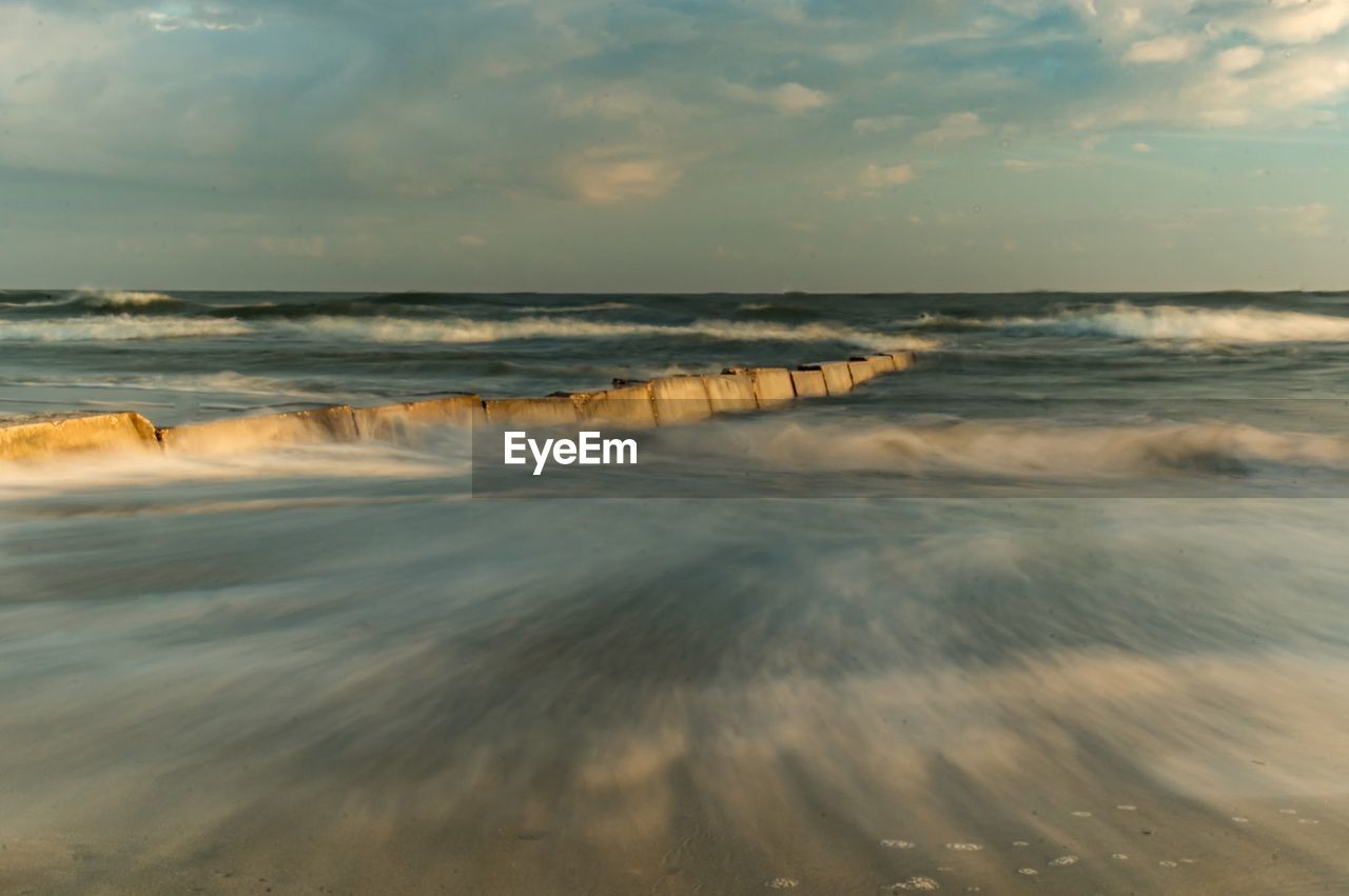 Long exposure of water in sea against cloudy sky during sunset