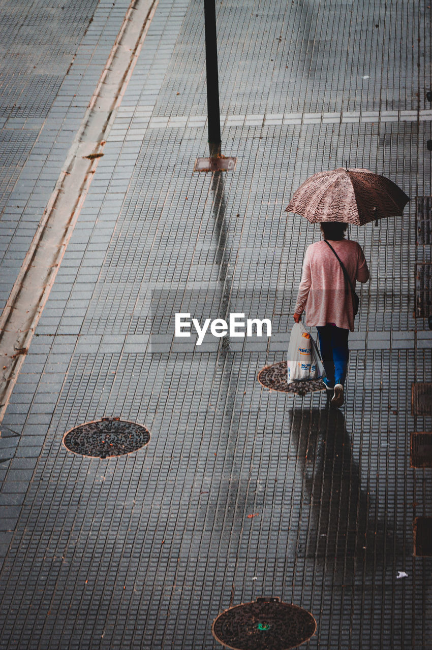 Rear view of woman walking on footpath with an umbrella. rain