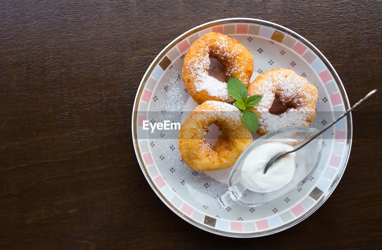 Three donuts with powdered sugar, green mint leaf and sour cream on plate. wooden background .