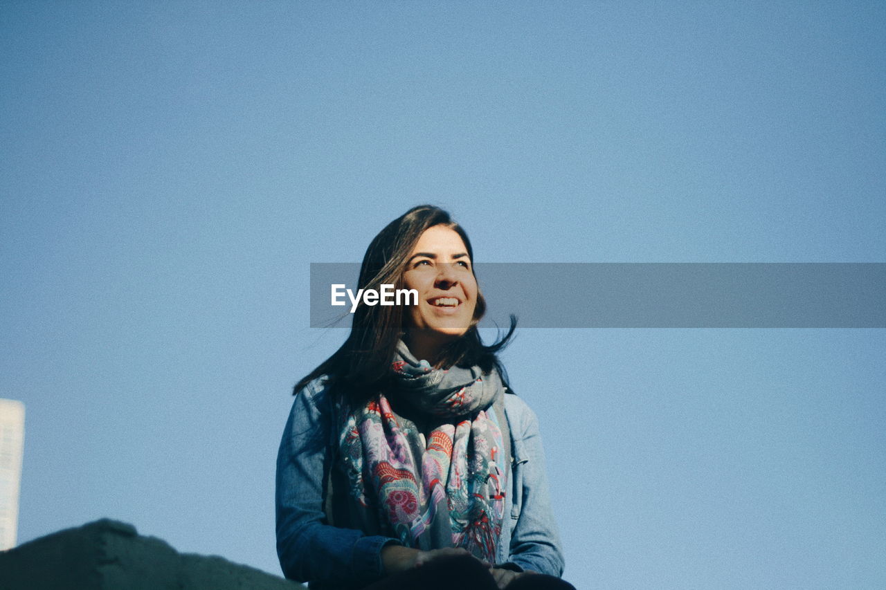 Smiling young woman sitting against clear blue sky