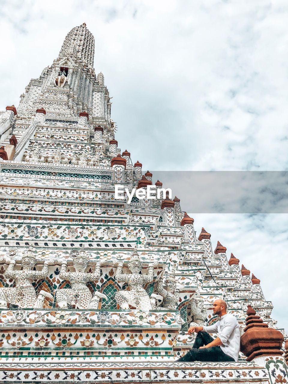 Man sitting on ornate temple roof against cloudy sky