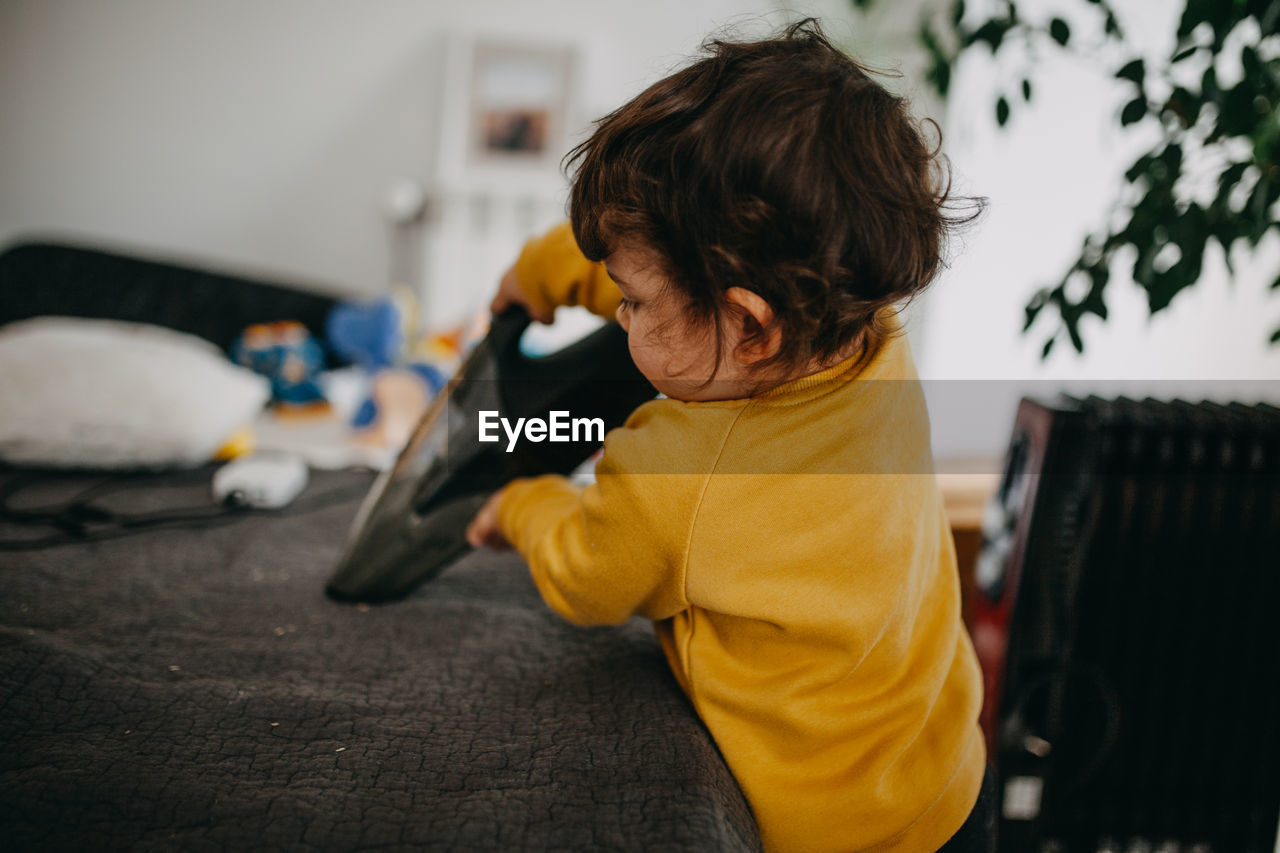 Rear view of child with vacuum cleaner at home