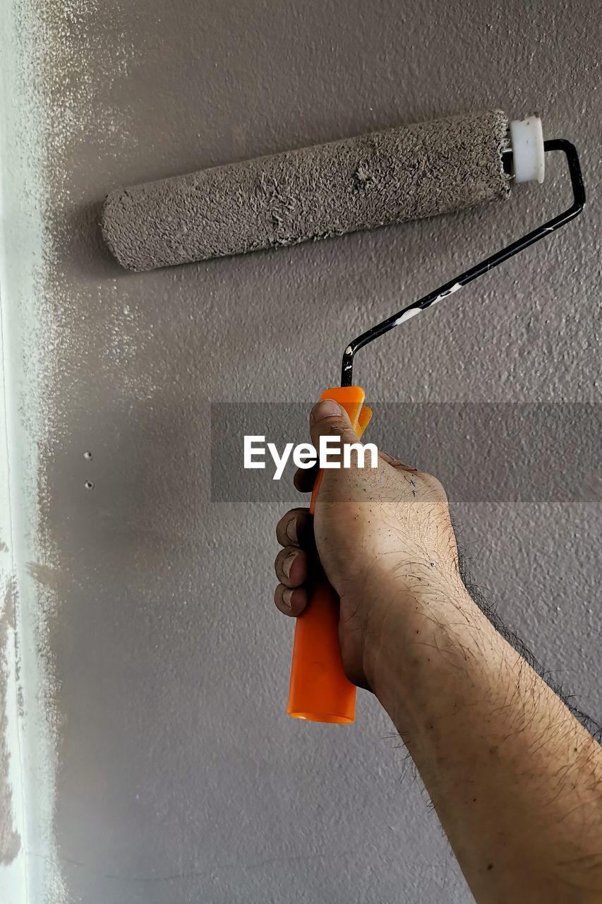 CLOSE-UP OF MAN HOLDING ORANGE AGAINST WALL