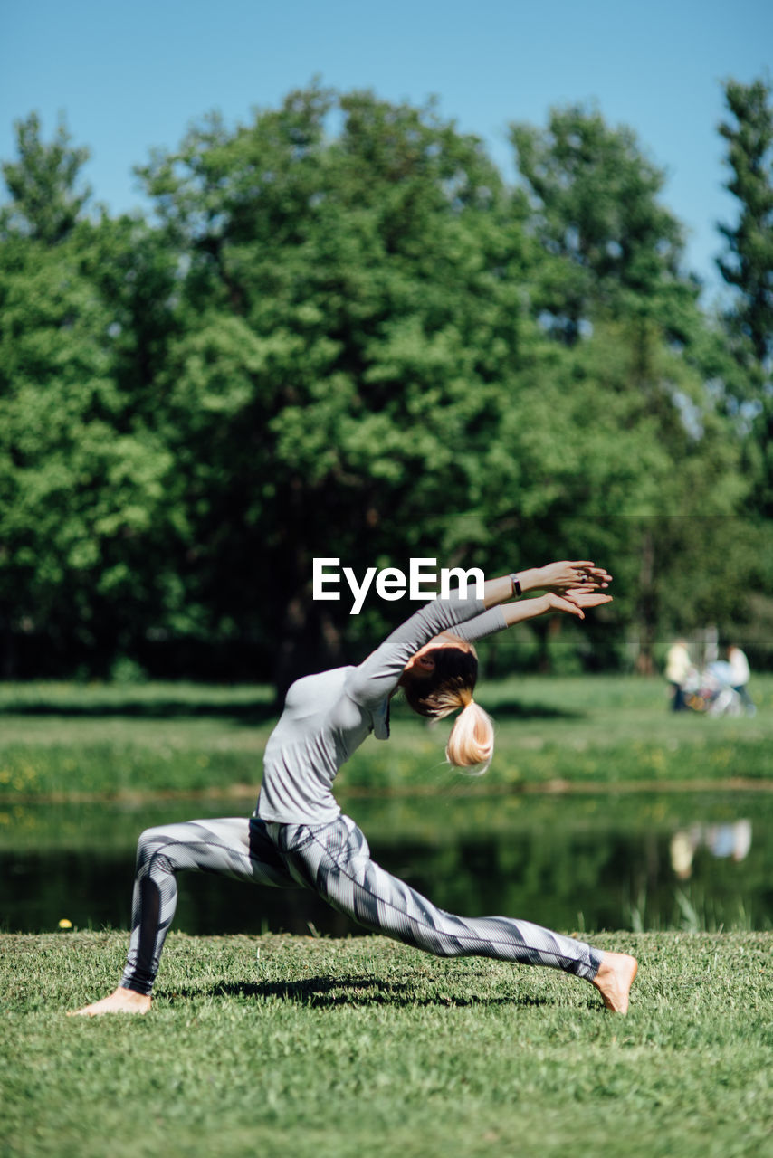 Full length of young woman exercising by pond on field