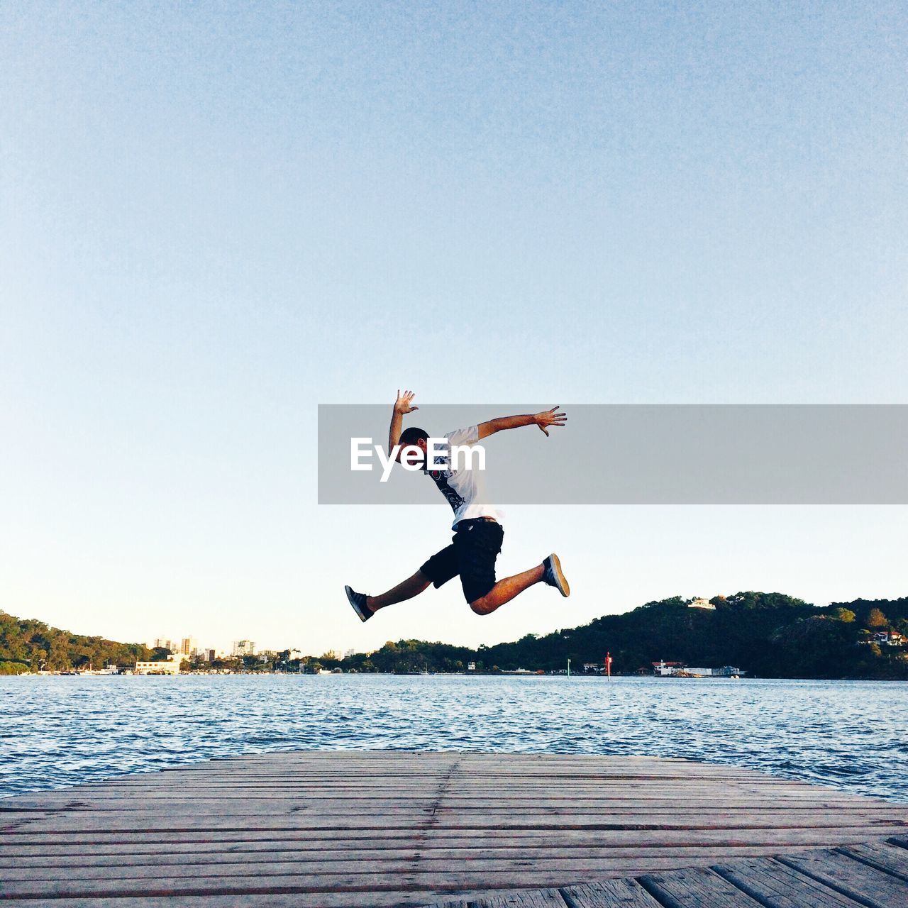 Man in mid-air over pier and sea against clear sky