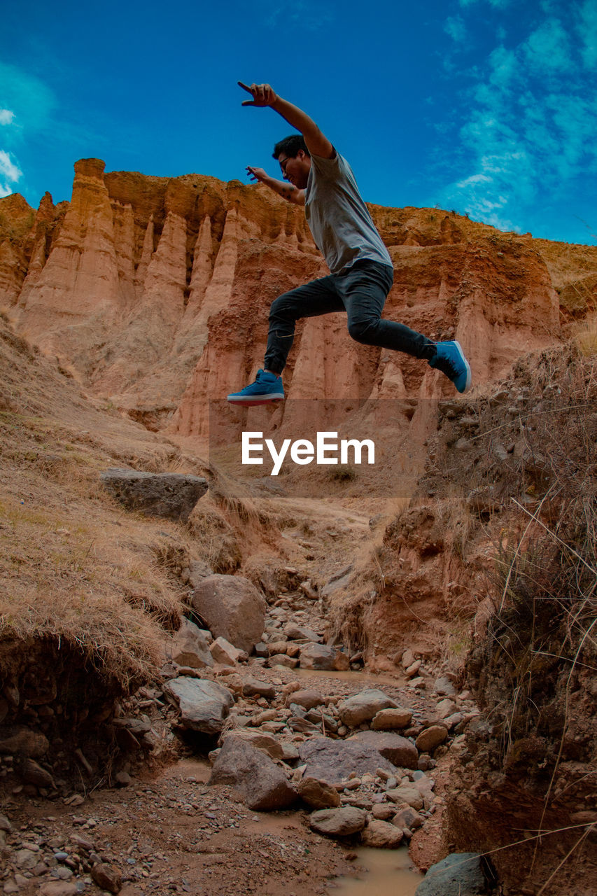 LOW ANGLE VIEW OF MAN CLIMBING ROCK