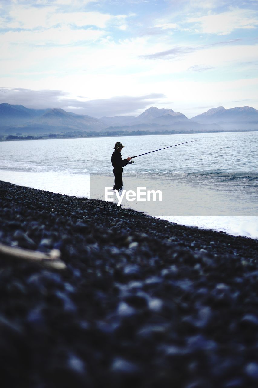 Silhouette man fishing on sea against sky