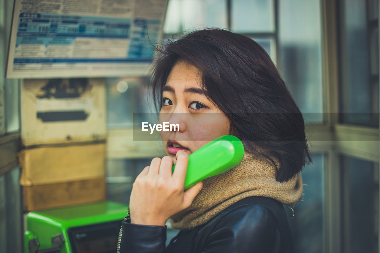 Portrait of young woman talking over telephone in booth