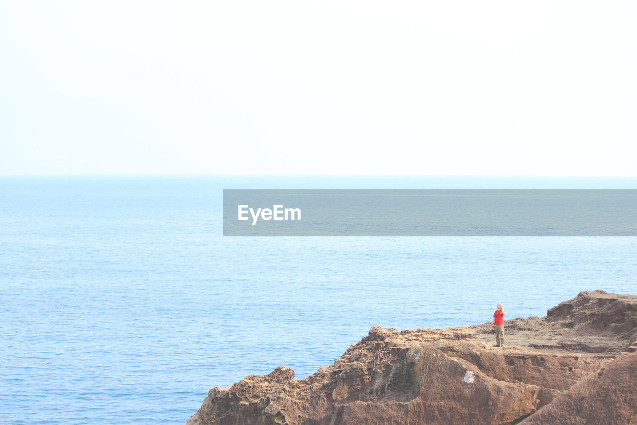 Distant view of man standing on rocky mountain against sea
