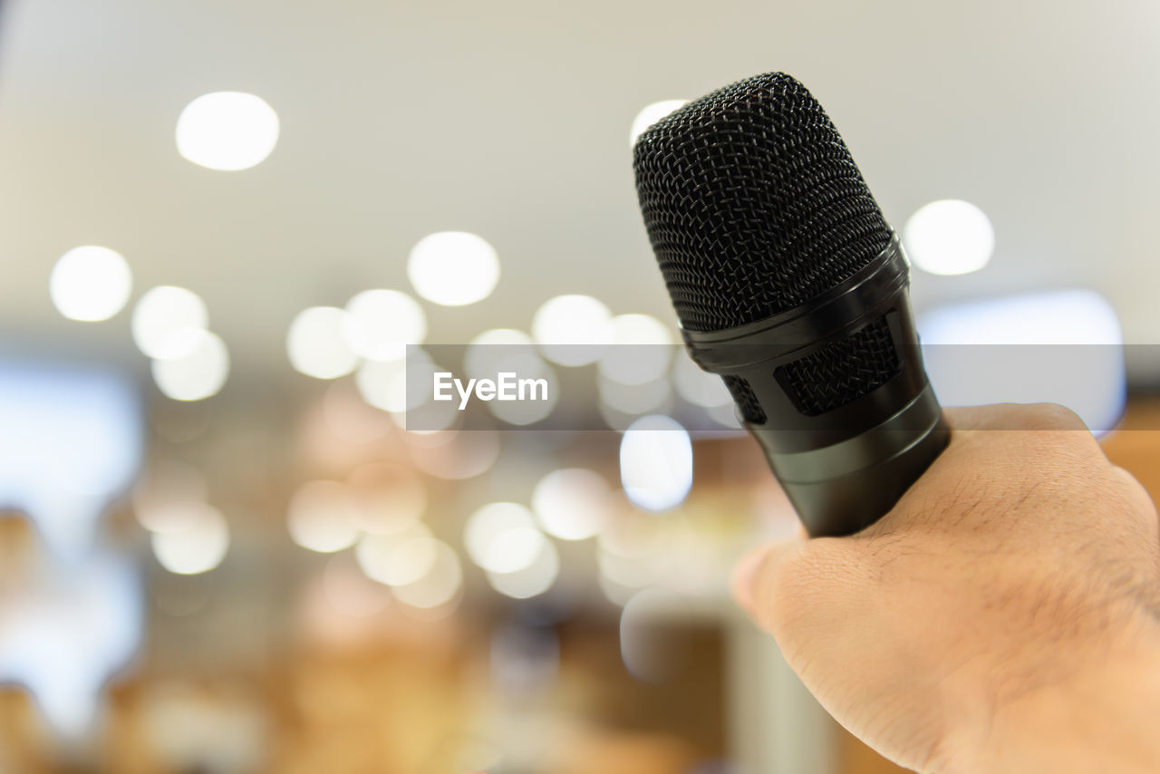 Cropped hand of person holding microphone against defocused lights