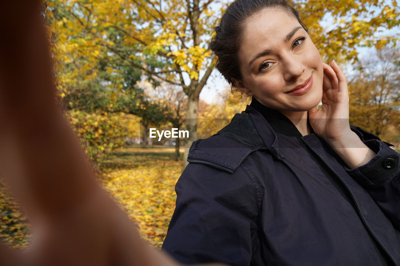 PORTRAIT OF SMILING YOUNG WOMAN WITH AUTUMN TREES