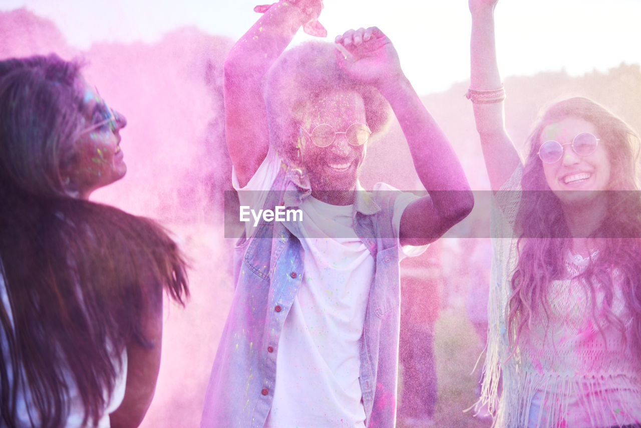 Friends playing with powder paint against sky